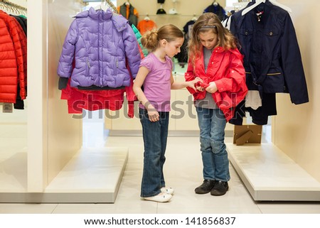 Two modern girls try on clothes in a store children clothes