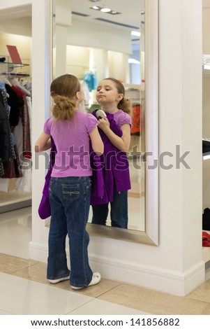 Little girl near a mirror try on clothes in a store children clothes