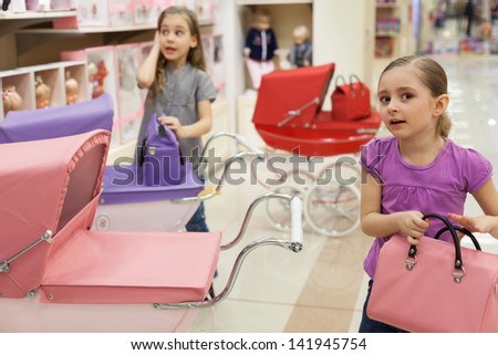 Two girls in a toy store with a rows of dolls purchased a buggy and handbag