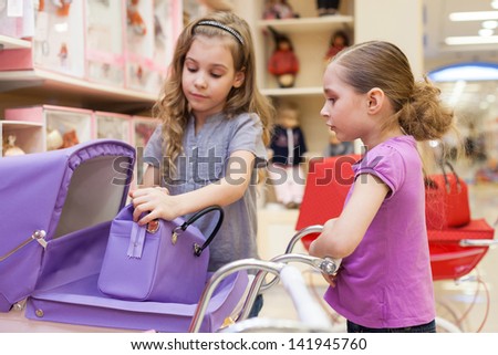 Two girls in a toy store with dolls purchased a buggy and handbag, focus on right girl