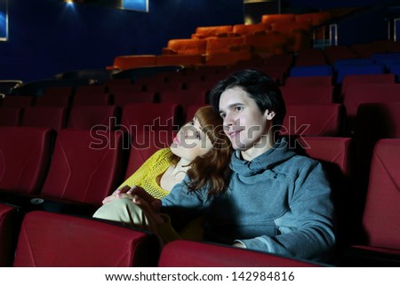 Young man and woman watch movie, embrace and smile in cinema theater.