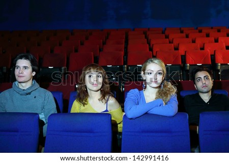 Four young friends watch movie in cinema theater. Focus on girls.