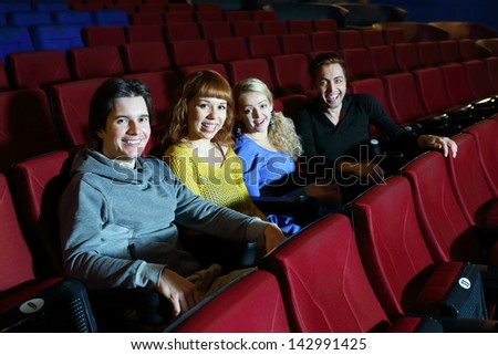 Two happy young couples look at camera and laugh in cinema theater. Focus on left pair.