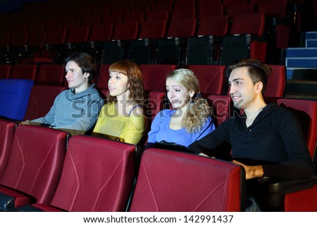 Four young people watch movie in movie theater. Focus on girls.