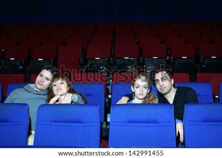 Four young people (two pairs) watch movie in cinema theater.