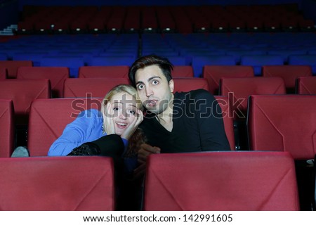 Young man and woman watch movie and press close to one another in fright in cinema theater.
