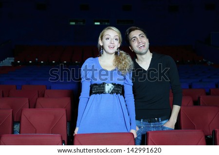 Young man and woman stand, watch movie and laugh in cinema theater.