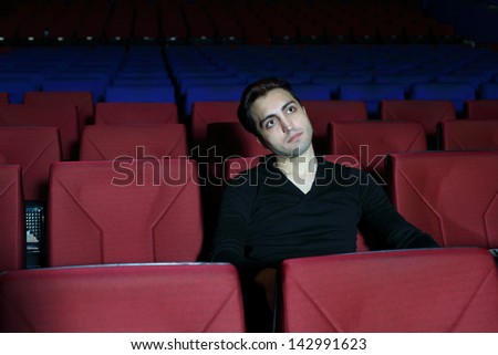 Young serious man in black watches movie in big cinema theater.