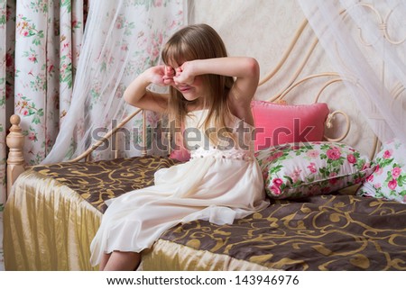 Little girl sitting on the bed and rubs his eyes before going to sleep