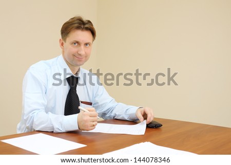 Smiling businessman sit at table and signs documents in office.