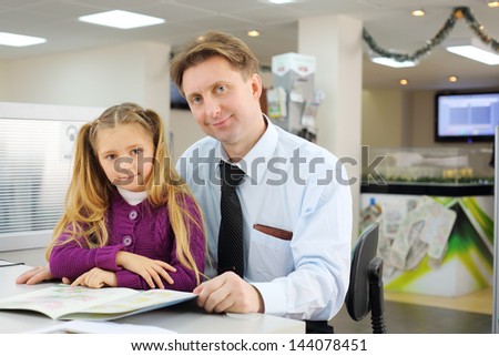 Happy girl and her father with floor plan booklet in office. They choose apartment.