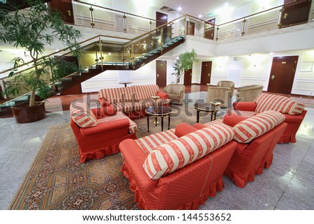 Atrium with red soft armchairs, couches and stairs in stylish hotel.