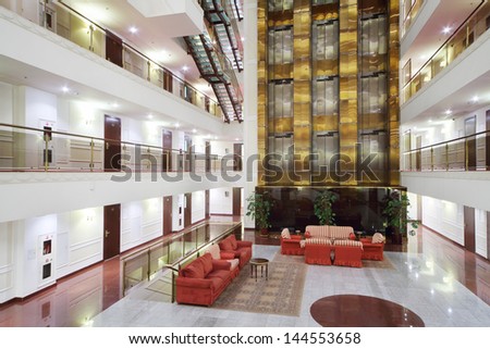Atrium With Red Armchairs, Couches And Elevators In Stylish Hotel.