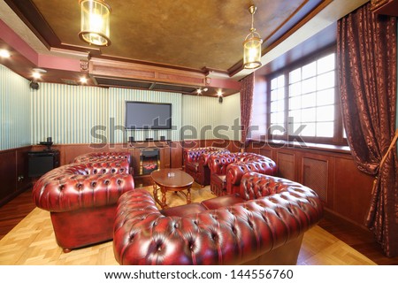 English cigar room with red leather armchairs and home theater system.