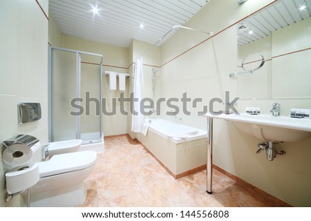 Light and empty bathroom with white bath, toilet and shower cabin.