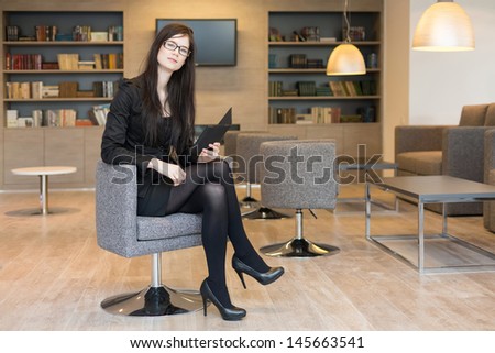 Business woman in glasses sits on a chair with notepad in the office