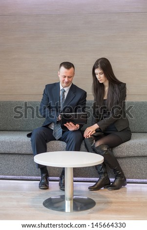 Man and girl in business suits sitting on the sofa next to the table