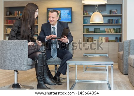 A girl with a man in a suit sitting on a chair and discuss business