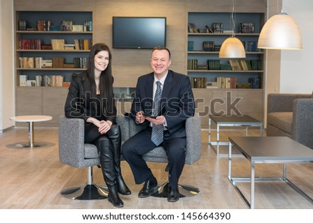A smiling girl and man in business suits sitting on chairs with notepad