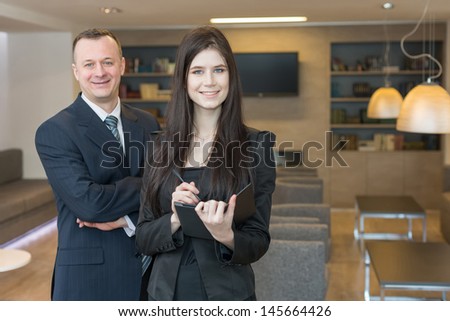 Smiling man and woman in business suits standing in office room, focus on a woman.