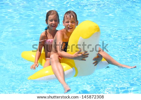 Happy girl and boy swim at the children inflatable toy in the swimming pool