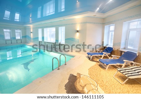 Beautiful clean pool with images of dolphins at bottom and sunbeds in big room.