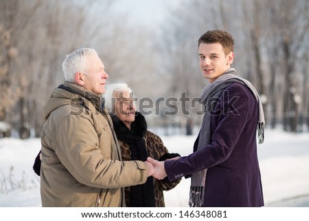 The young man greets an elderly couple in the park in winter