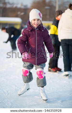 Little girl in knee pads skating at the rink in winter