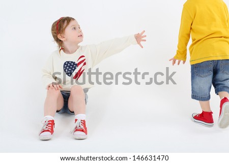 Little cute girl sits on floor and reaches out to boy going past on white background.