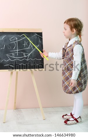 Little girl shows by yellow pointer ship at chalkboard in studio.