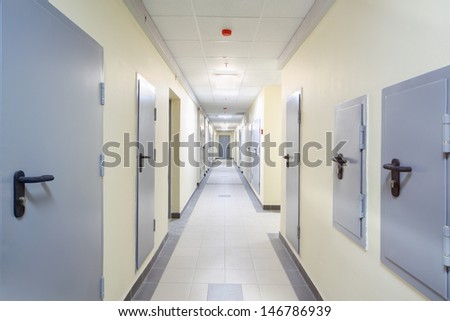 Long yellow hallway with grey metal doors and floor covered by tiles.