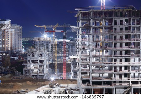 High multi-storey buildings under construction and cranes at night.