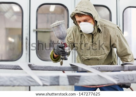 Man in protective clothes and respirator works in paint-spraying booth, painting car details