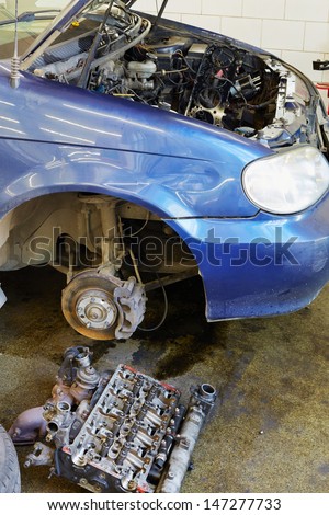 MOSCOW - AUG 22: Engine cylinder head lies on floor near car under repair with open hood and dented fender in workshop of Service station Avtostandart, August 22, 2012, Moscow, Russia.