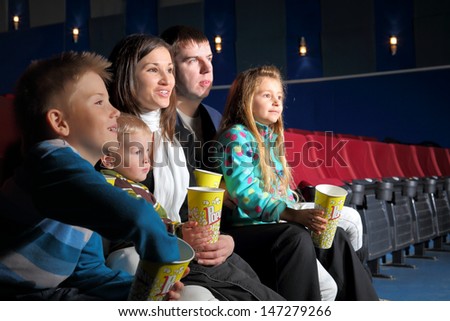 Friendly family with interest watching a movie and eating popcorn in the cinema