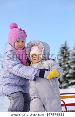 Older sister hugs baby dressed in warm clothes outdoor at winter.