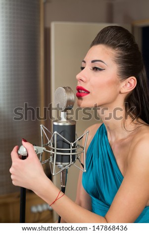 Beautiful woman with red lips sing in room with microphone in Recording Studio