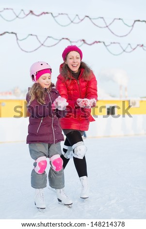 Happy mother and daughter mold snowballs at outdoor skating rink in winter