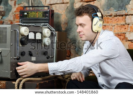 Man in big white headphones configures power source to radio receiver in very old house.