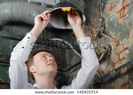 Handsome man in white shirt changes light bulb in very old house.