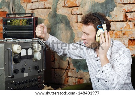Man in big white headphones knocks on power source to radio receiver in very old house.