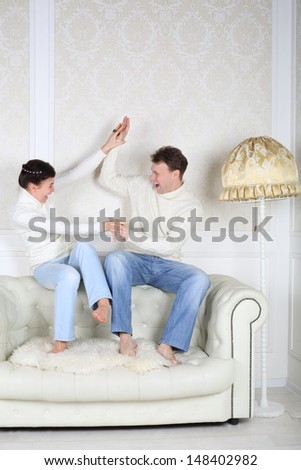 Happy husband and wife sits on back of white leather sofa and fight at home.