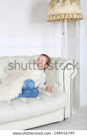 Little girl sleeps under white skin on white sofa in white room at home.