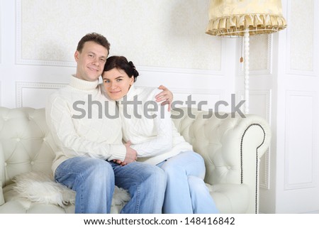 Happy husband and wife hug and look at camera on white sofa at home.