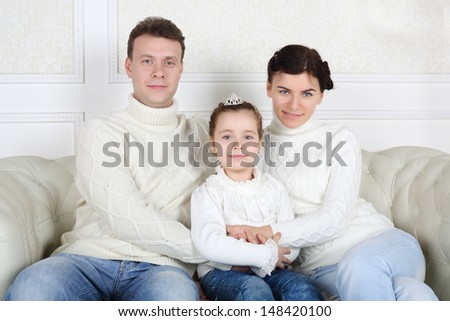 Father and mother hugs little daughter and sit on sofa at home.