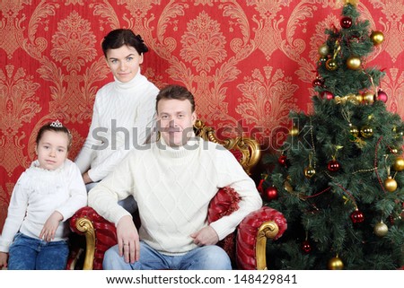 Happy family in white sweaters and jeans near Christmas tree in red room.