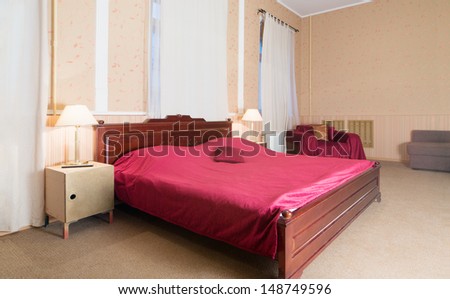 The simple interior bedroom with a bed, a bedside table and chairs