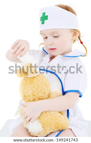 Little girl dressed as nurse bandages head to toy rabbit isolated on white background.