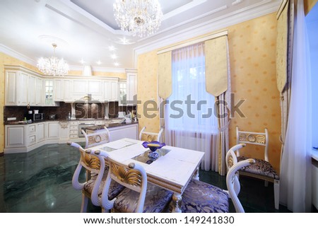 Kitchen with luxury furniture in classic style, marble floor and small dining table.