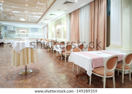 Small round and square tables with tablecloths in restaurant of modern hotel.